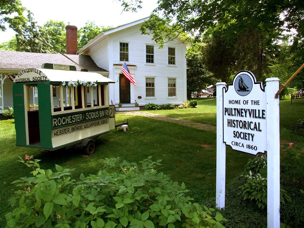 Summertime exterior image of an early 19th century building with Willaims-Pultneyville Historical Society sign out front